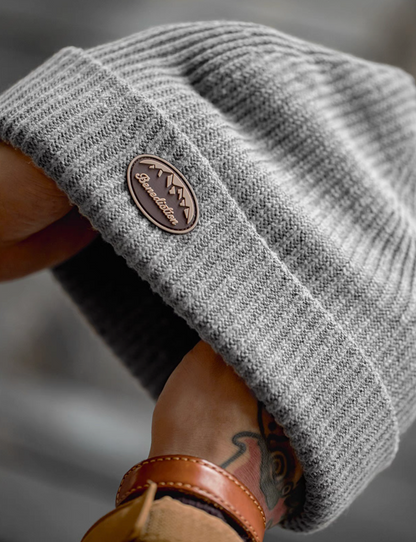 Close-up of Classic Ribbed Knit Beanie with Logo Detail in gray showing soft ribbed knit texture and embossed logo patch on folded brim