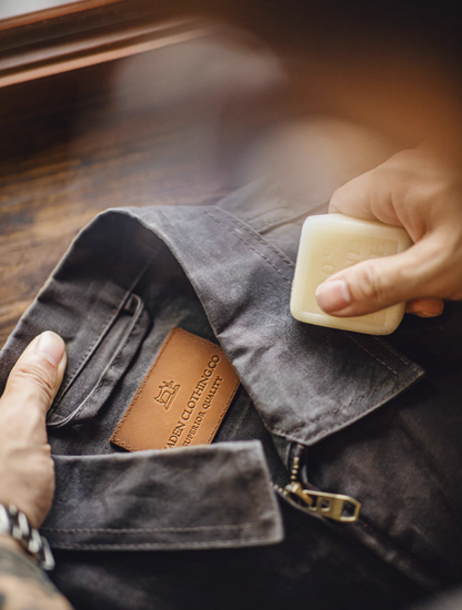 Pewter Gray Classic Trail Waxed Jacket being treated with wax block, showing jacket care and reproofing process