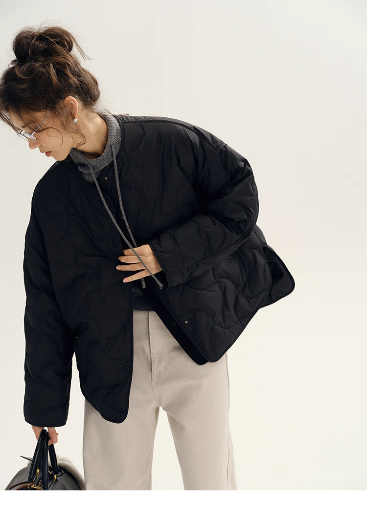 Black quilted down jacket shown from side as model adjusts front opening.
