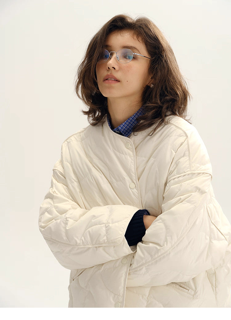 Closeup of ivory white quilted down jacket showing wave-pattern stitching and snap front.