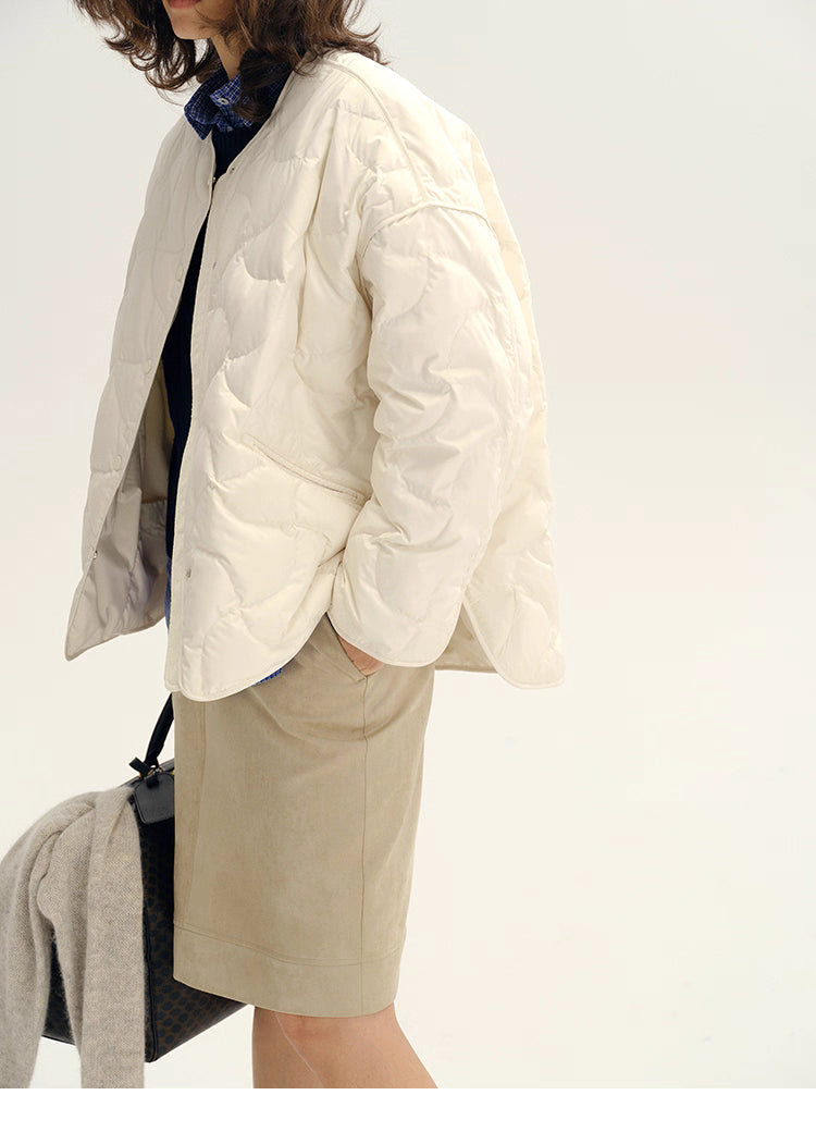 Side view of ivory white oversized quilted jacket styled with beige skirt and bag.