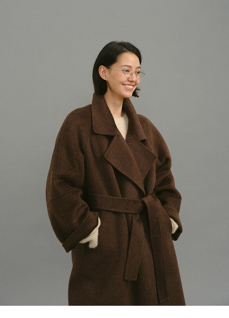Three-quarter view of belted dark coffee wrap coat with relaxed oversized sleeves.