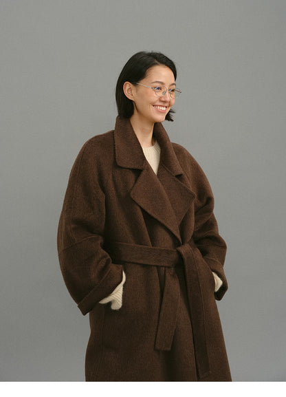 Three-quarter view of belted dark coffee wrap coat with relaxed oversized sleeves.