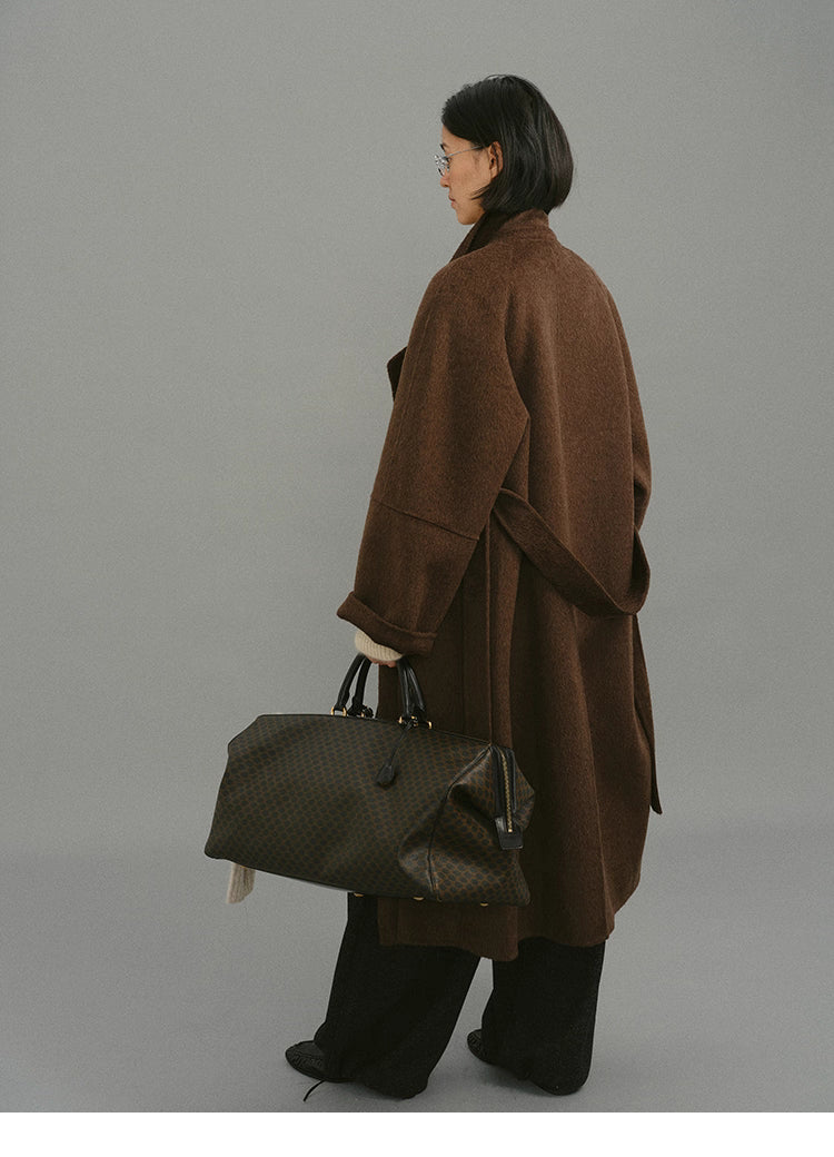 Back three-quarter view of camel-blend coat with model holding patterned travel bag.