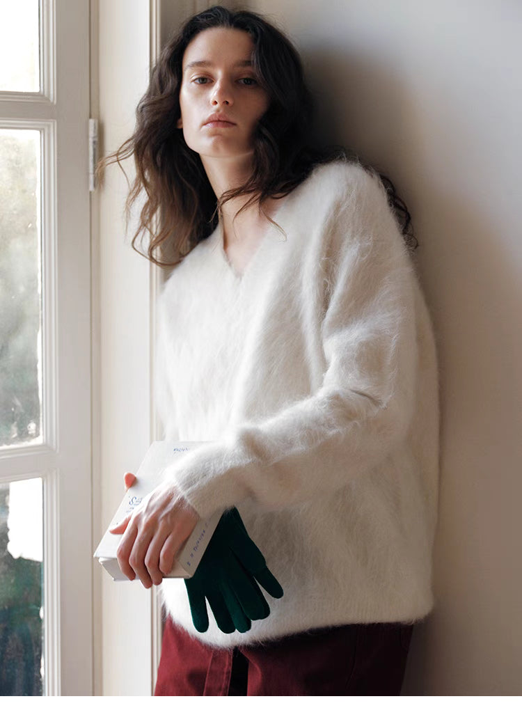 Cloud white wool sweater leaning against wall holding book showcasing relaxed fit and cozy styling