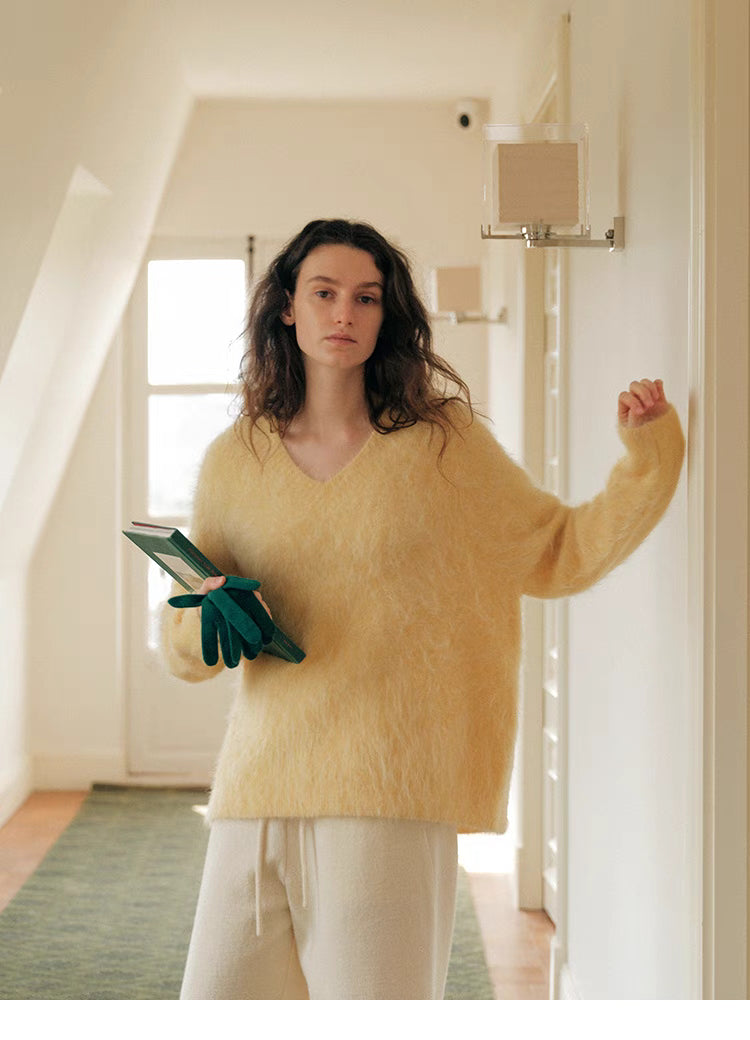 Cream yellow V neck wool sweater standing in hallway holding book highlighting airy texture and drop shoulder design