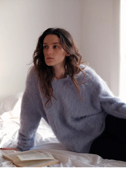 Misty blue wool sweater sitting on bed with relaxed pose highlighting lightweight warmth and soft fabric