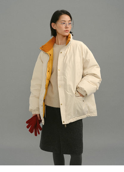 Full-body shot of model in a cream yellow down coat with mustard inner collar, holding red gloves by her side.