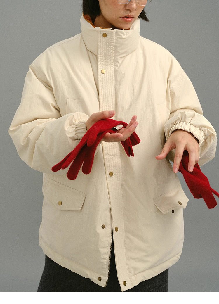 Front view of model wearing cream yellow coat with the stand collar raised, holding red gloves.
