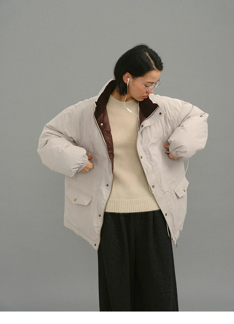 Model in a light greige down coat listening to earphones while looking downward.