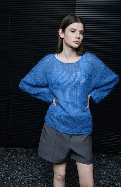 Model in Cobalt Blue semi-sheer floral knit pullover with hands on hips, paired with grey tailored shorts