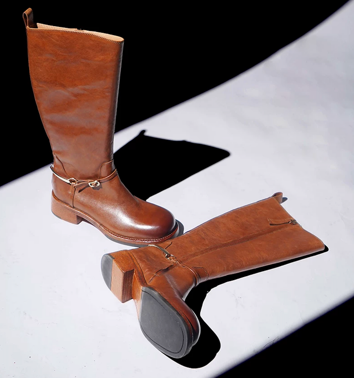 Cognac knee-high riding boots, one showing the leather sole with a rubber patch
