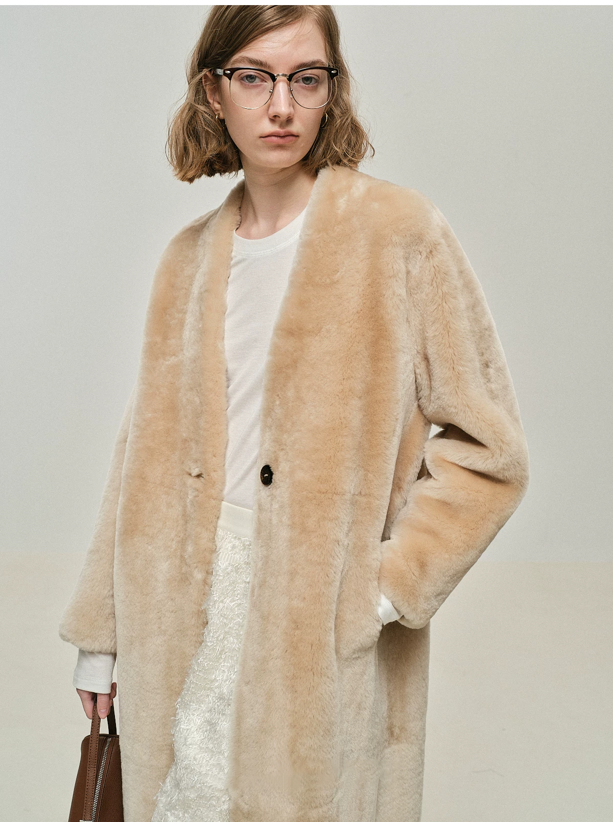 Close view of sand sheepskin shearling coat with collarless V-neck and single dark button