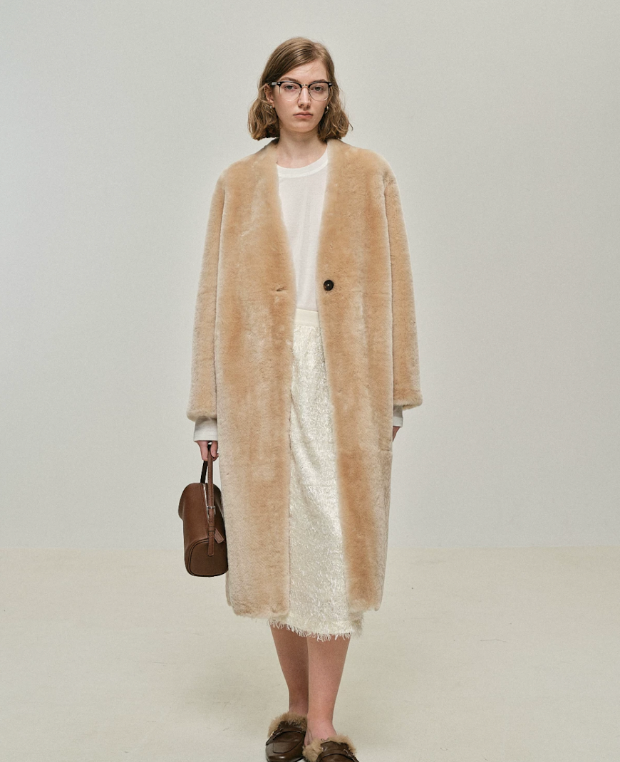 Full-length view of long sand shearling coat buttoned over a white tee and cream midi skirt