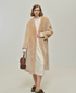 Sand collarless shearling coat worn open, showing straight below-knee length