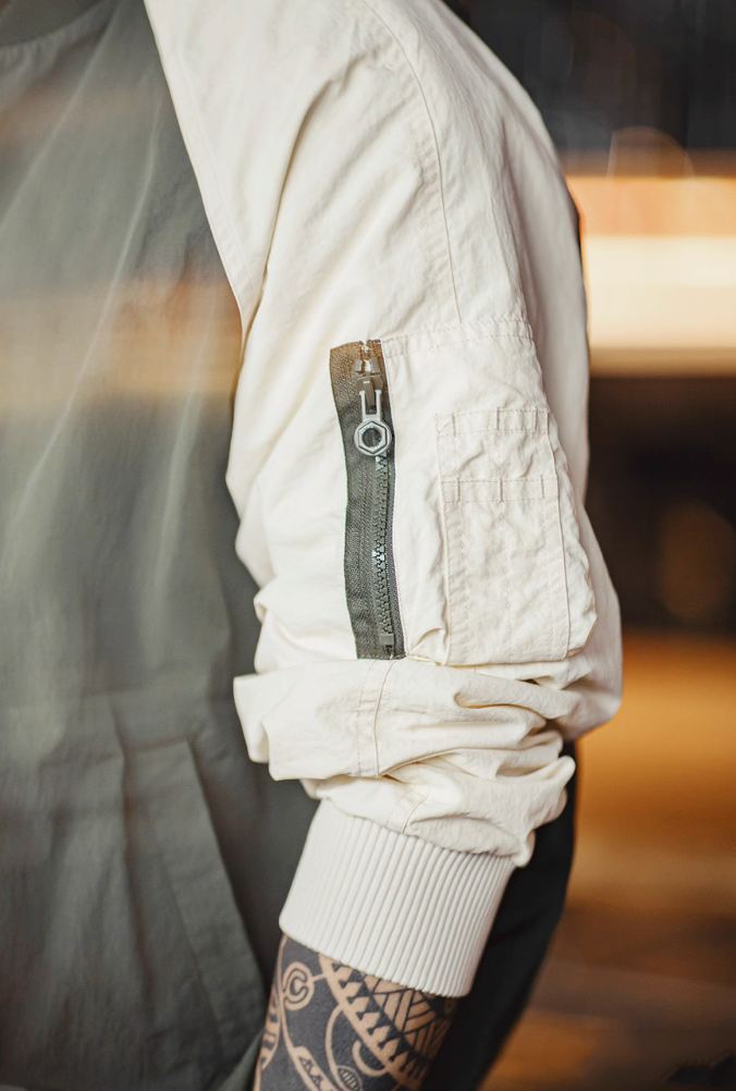 Close-up of utility sleeve zip pocket detail on cream arm