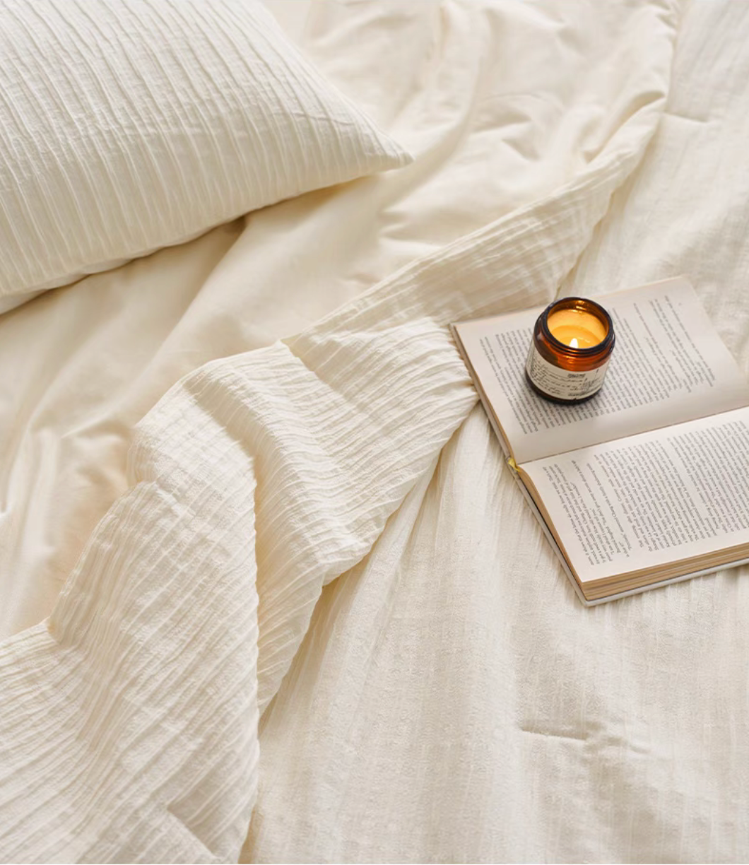 White Colorful cotton comforter and sham set close-up with candle, book, pillow sham, and textured cotton fabric