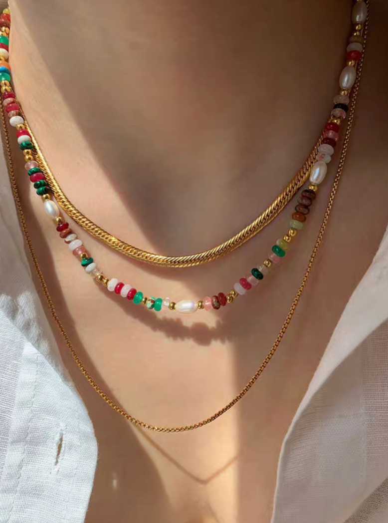 Multicolor gemstone and pearl necklace worn layered with gold chains, featuring vibrant beads and freshwater pearls for a chic look