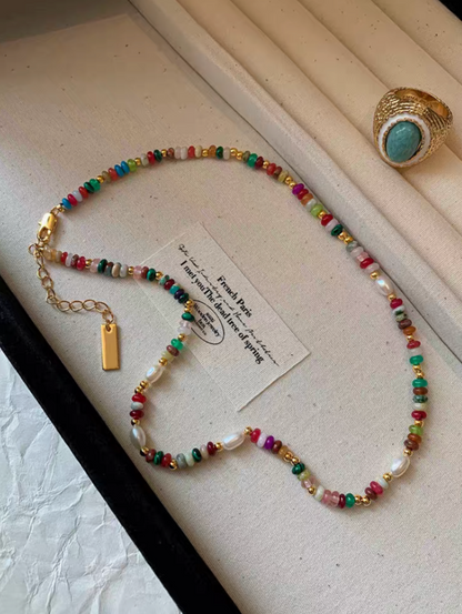 Close-up of colorful gemstone and pearl necklace with multicolor natural stones, glass beads, freshwater pearls, and gold-plated details on display surface
