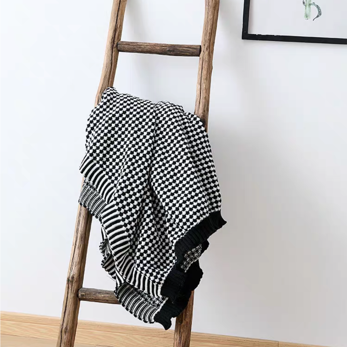 Black and white checkered acrylic knit throw blanket hanging on wooden ladder, modern minimalist decor