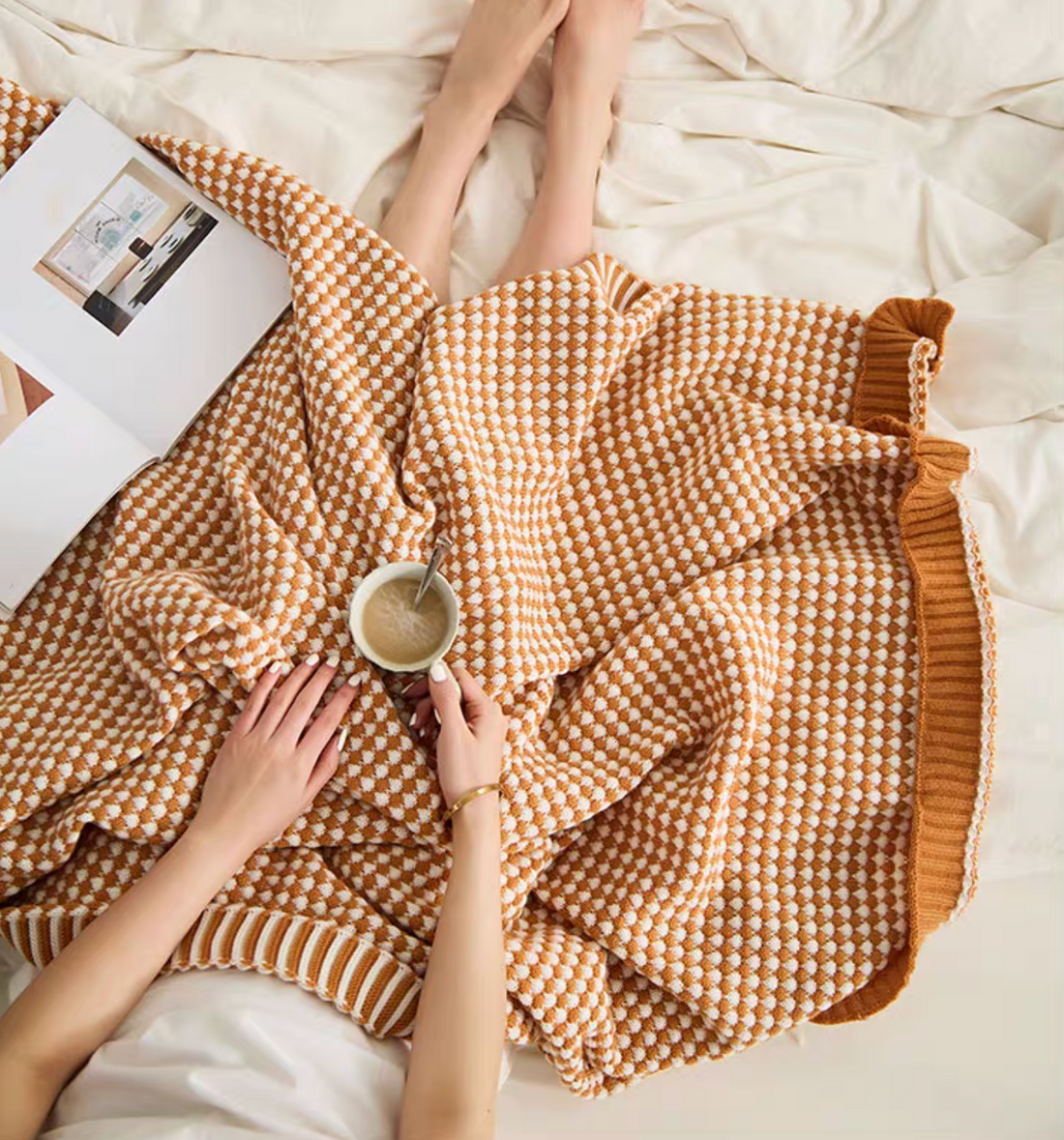 Woman relaxing under dark yellow checkered knit throw blanket on bed with coffee, soft cozy lifestyle scene