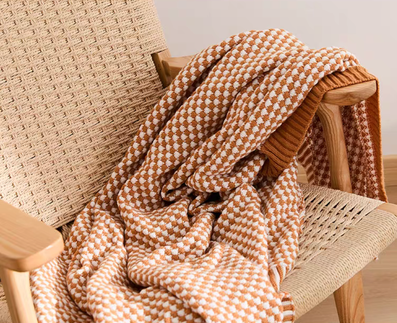Close-up of dark yellow acrylic knit throw blanket draped over woven chair showing soft textured pattern