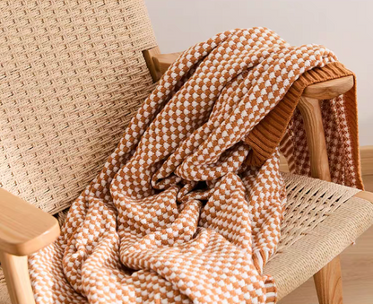 Close-up of dark yellow acrylic knit throw blanket draped over woven chair showing soft textured pattern