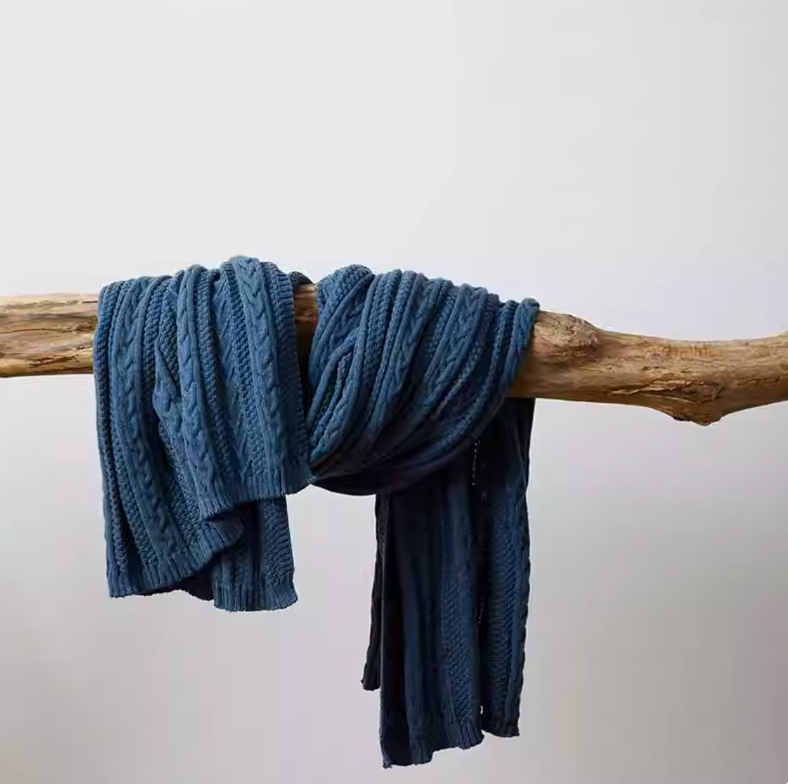 Dark blue braided knit oversized throw blanket spread across bed with soft folds creating a warm cozy bedroom look