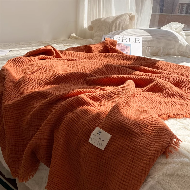 Close-up view of caramel organic cotton waffle gauze throw blanket showing soft textured weave on a bed.