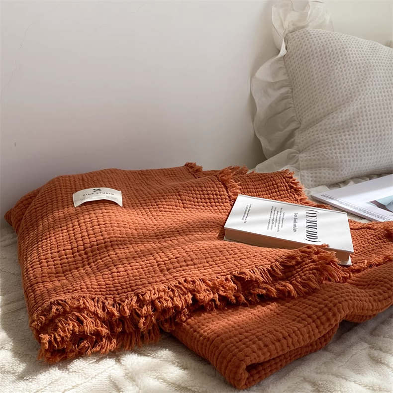 Folded caramel waffle textured organic cotton throw blanket with decorative fringe placed on soft bedding.