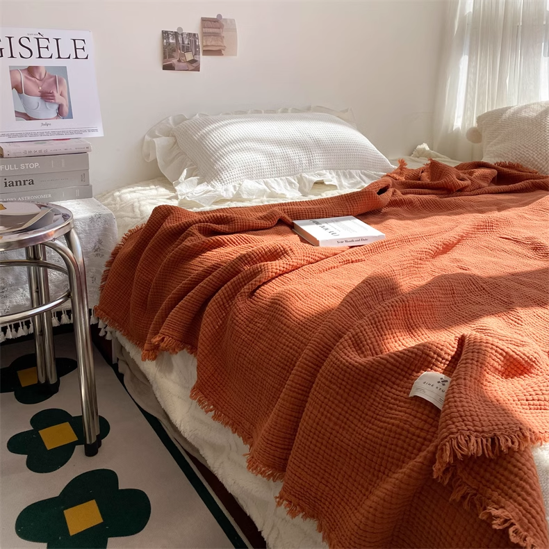 Caramel waffle textured organic cotton fringe throw blanket draped across a cozy bedroom bed with soft natural sunlight.