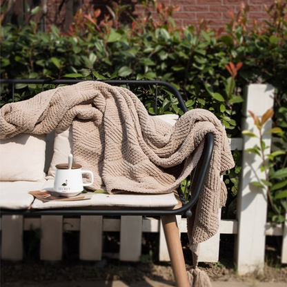 Almond chenille cable knit throw blanket draped across outdoor bench creating a soft warm and inviting seating area
