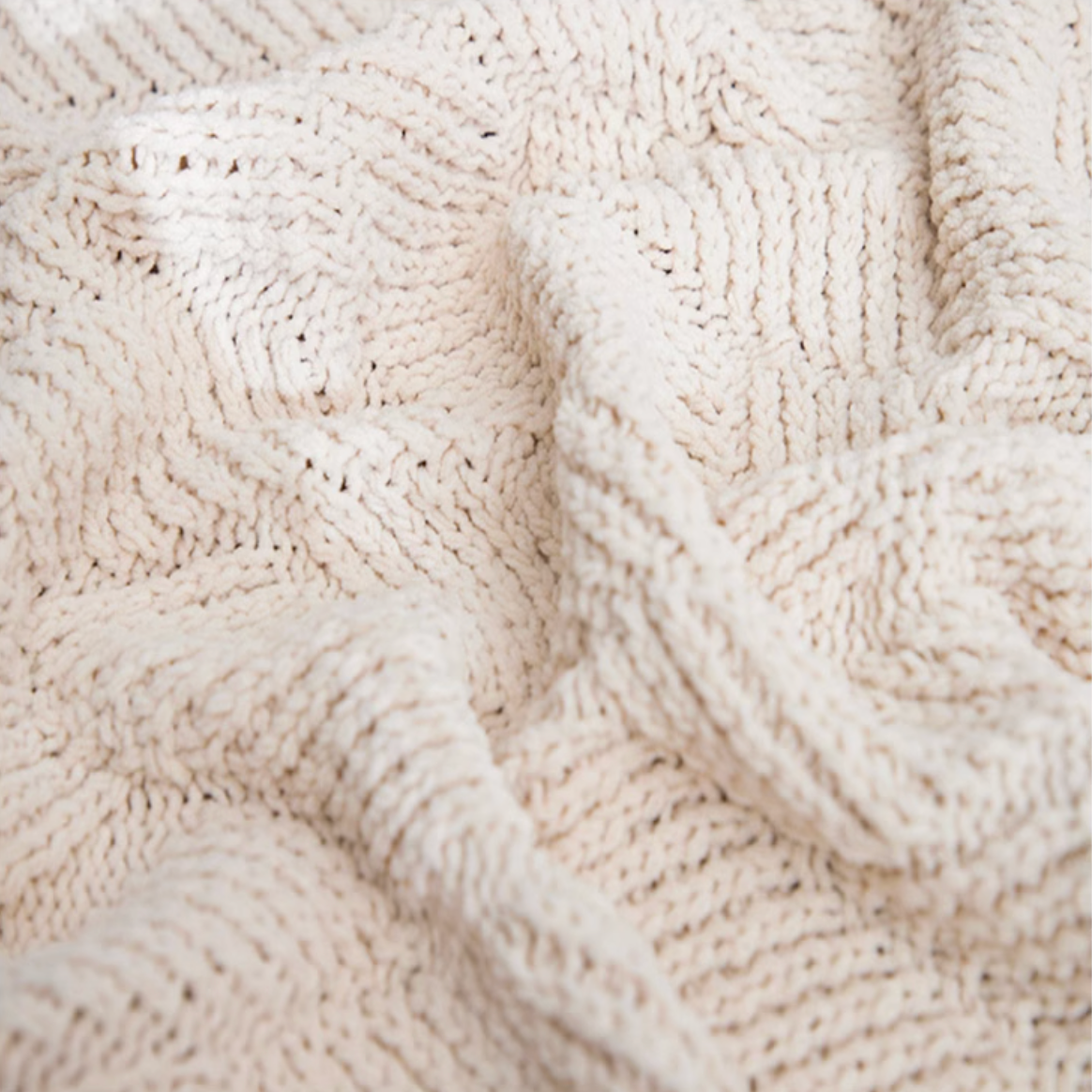 Close-up of beige chenille cable knit throw blanket highlighting thick soft yarn and detailed cable knit texture