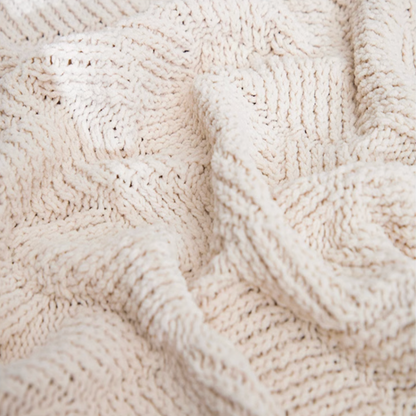 Close-up of beige chenille cable knit throw blanket highlighting thick soft yarn and detailed cable knit texture