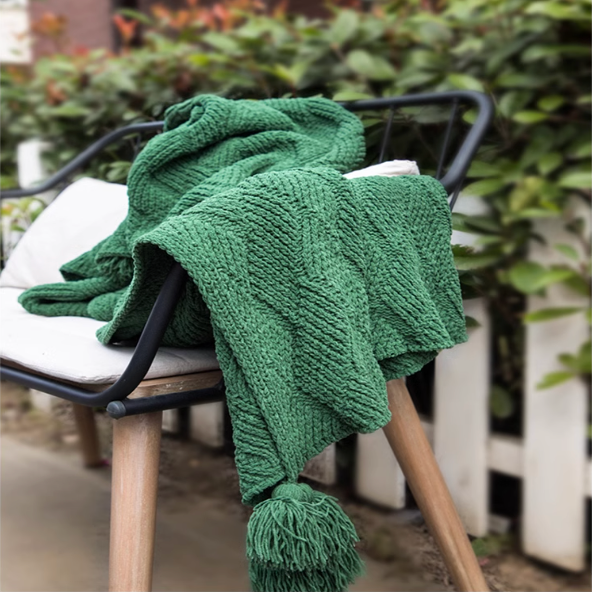 Green chenille cable knit throw blanket draped across outdoor bench creating a fresh natural cozy seating scene