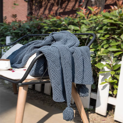 Navy blue chenille cable knit throw blanket draped over bench outdoors with natural greenery creating a cozy atmosphere