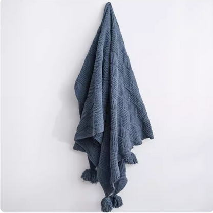 Navy blue chenille cable knit throw blanket hanging on wall with pom pom edges showing rich color and textured knit