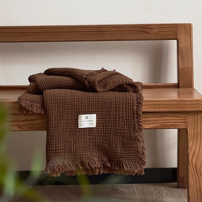 Chocolate brown organic cotton waffle throw blanket folded neatly on wooden bench with fringe detail.