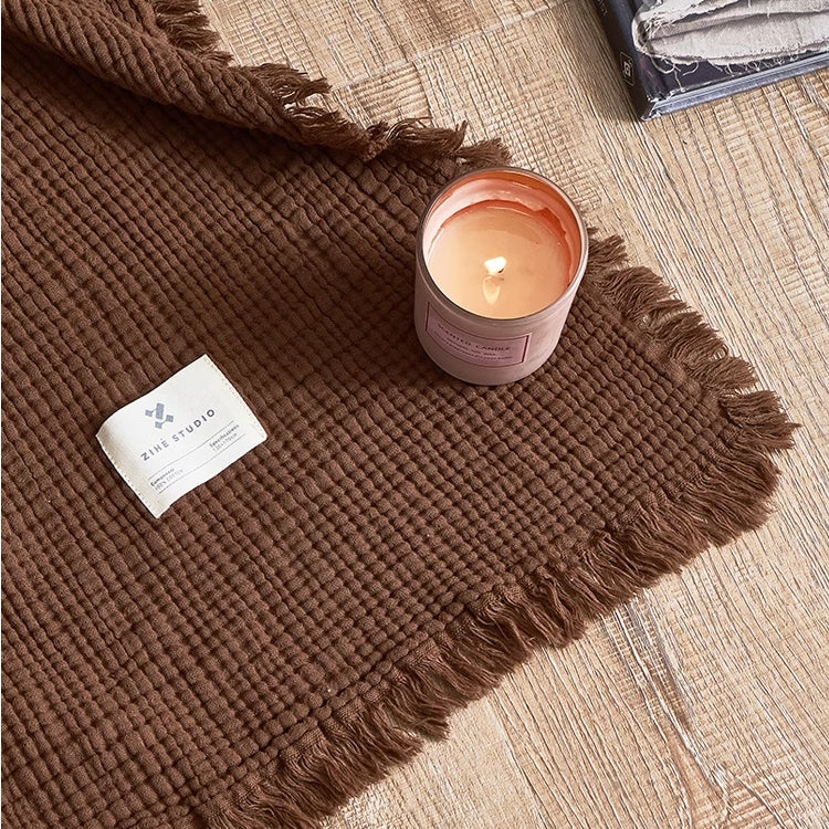 Close-up of chocolate brown waffle textured organic cotton throw blanket showing raw fringe edge and woven texture.