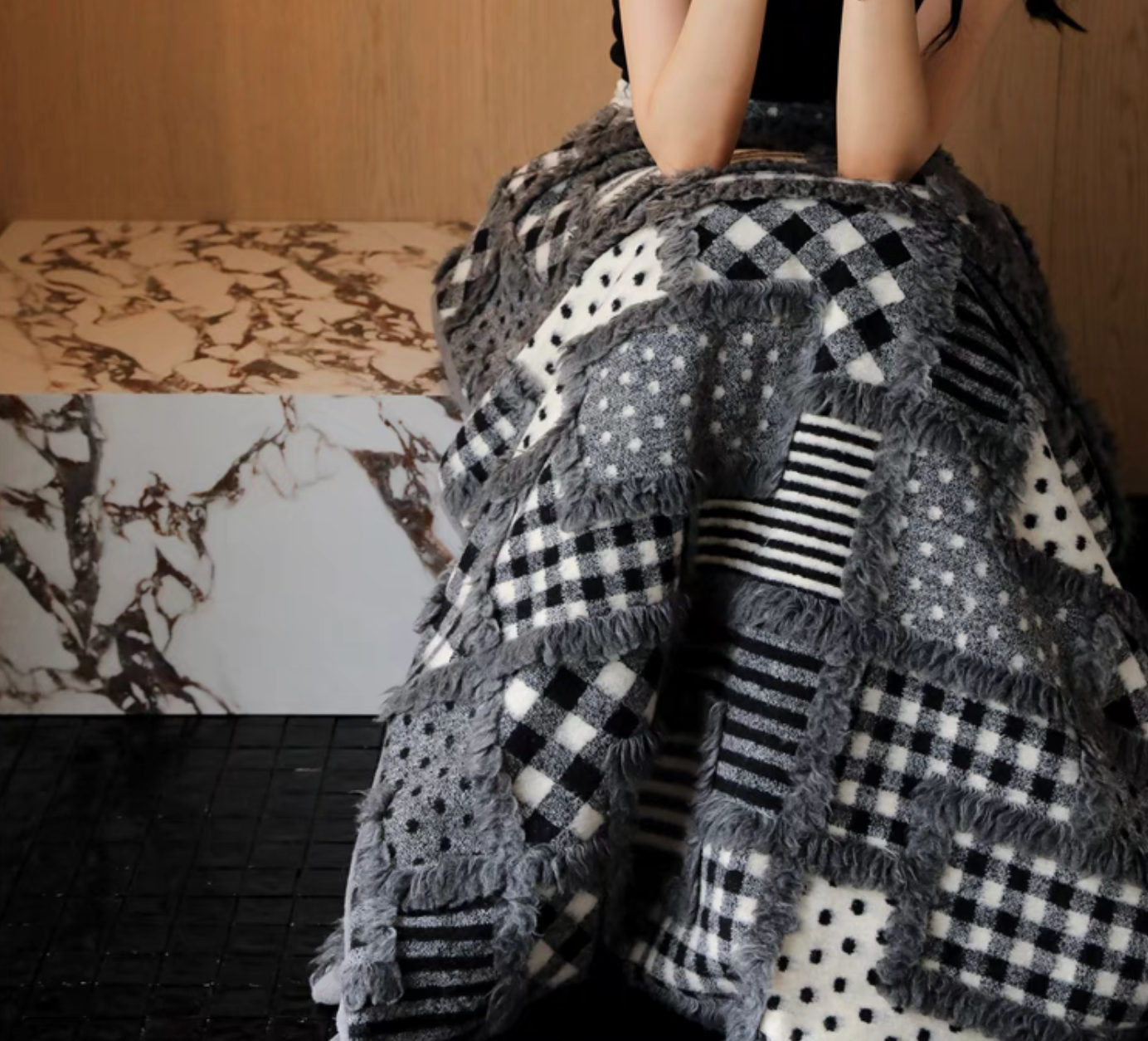 Person wrapped in gray checked patchwork throw blanket highlighting soft wool-blend texture and mixed geometric patterns