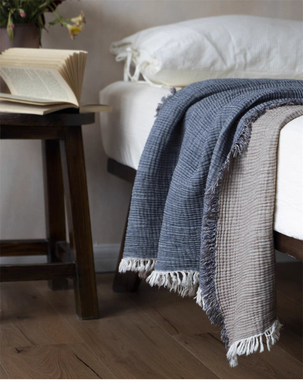 Gray khaki reversible cotton throw blanket draped over bed edge beside wooden nightstand in minimalist bedroom