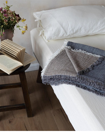 Reversible gray khaki cotton gauze throw blanket folded on bed showing two-tone design and soft fringe trim