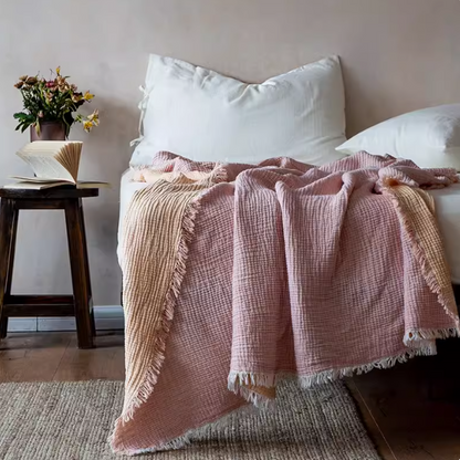 Orange pink reversible cotton gauze throw blanket layered on bed with soft waffle texture and fringe edges