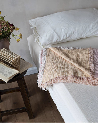 Reversible orange pink cotton gauze throw blanket folded on bed showing two-tone summer blanket design