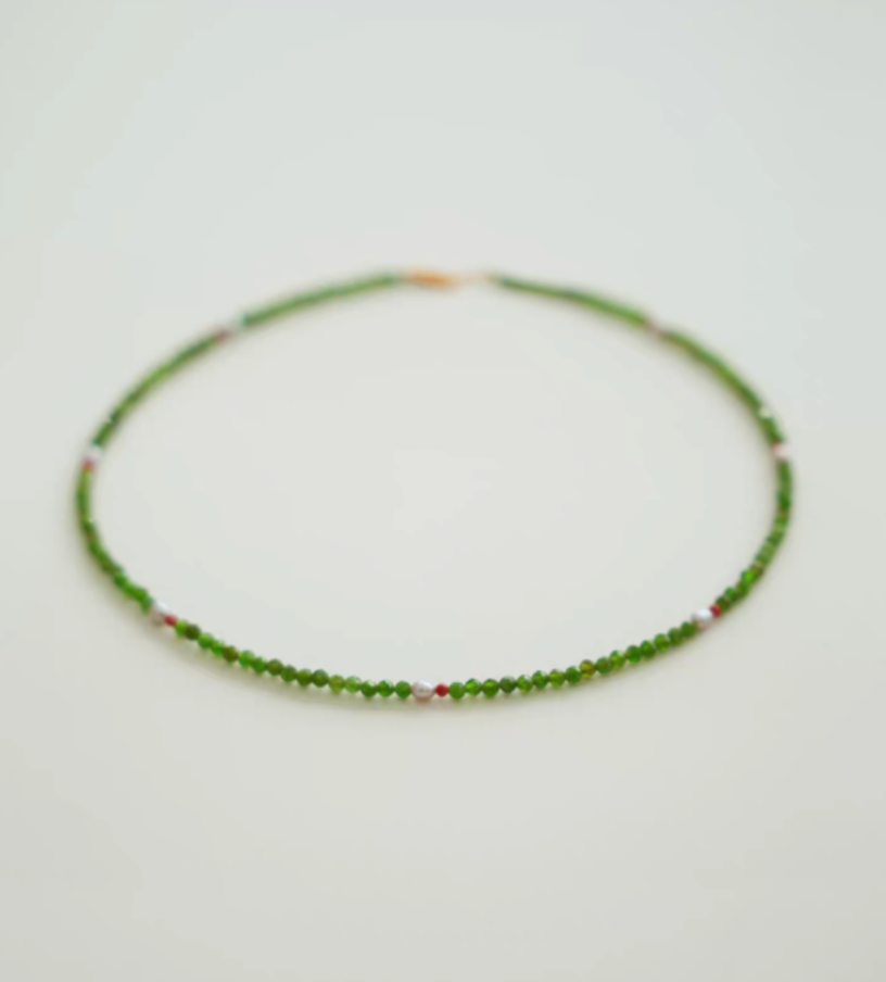 Flat lay of emerald green gemstone necklace with diopside beads, freshwater pearl center, and red agate spacer details