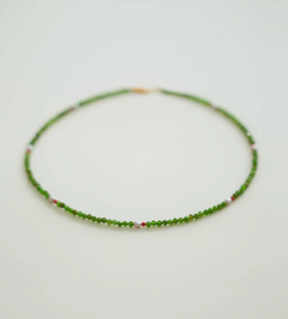 Flat lay of emerald green gemstone necklace with diopside beads, freshwater pearl center, and red agate spacer details