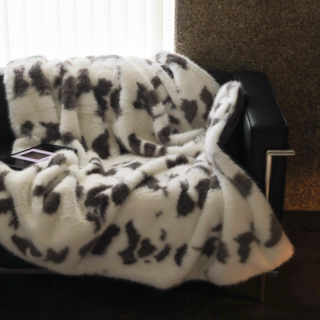 Cow cream faux fur throw blanket draped over modern sofa showing fluffy long pile texture