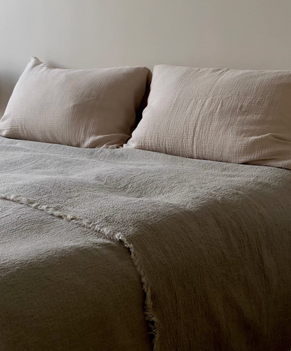 Close up of handcrafted raw edge fringe detail on classic natural French flax linen duvet thin quilt showing textured stonewashed linen fabric