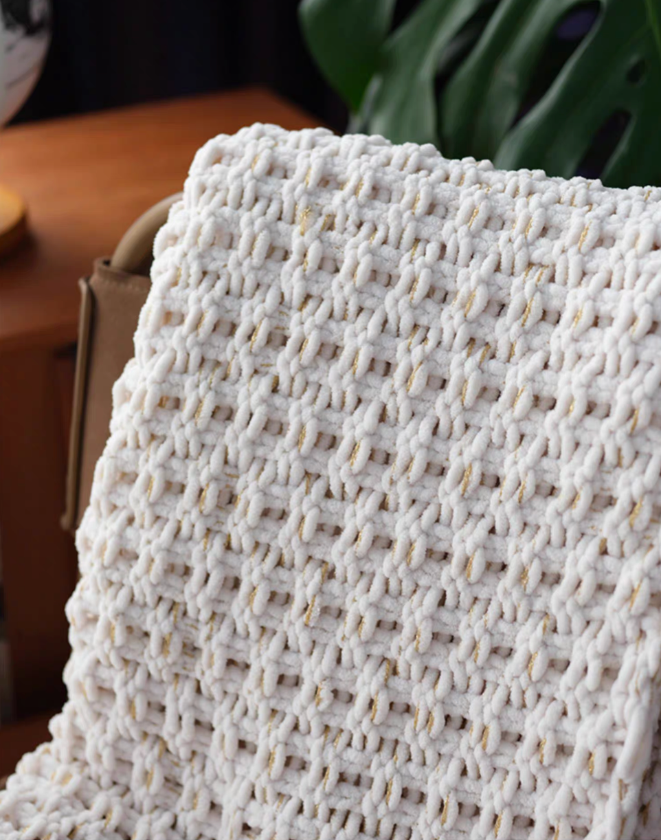 Close-up of white chunky knit throw blanket folded over chair back showing thick woven chenille texture