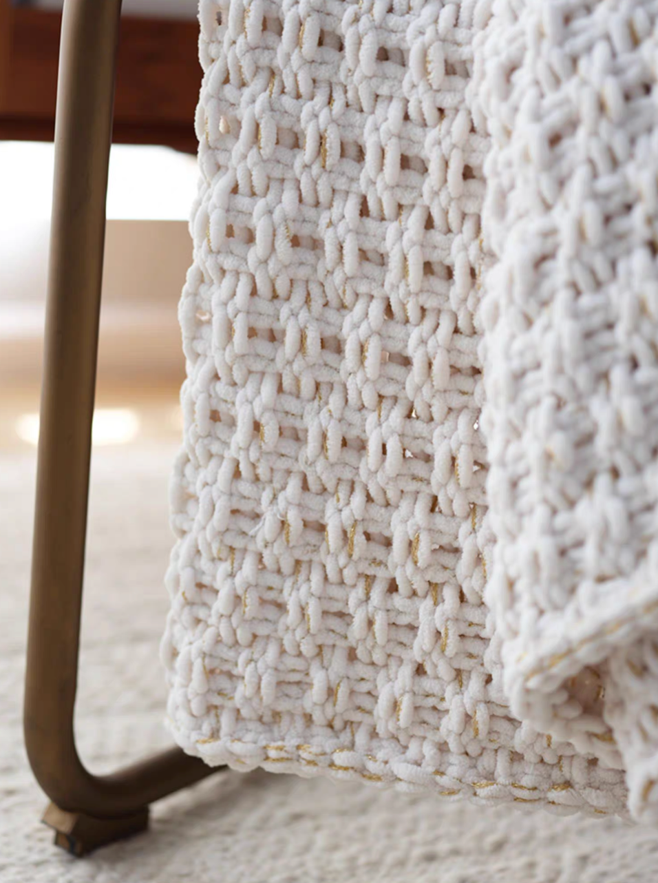 Side view of white chunky knit throw blanket hanging over chair with detailed woven texture and soft chenille finish